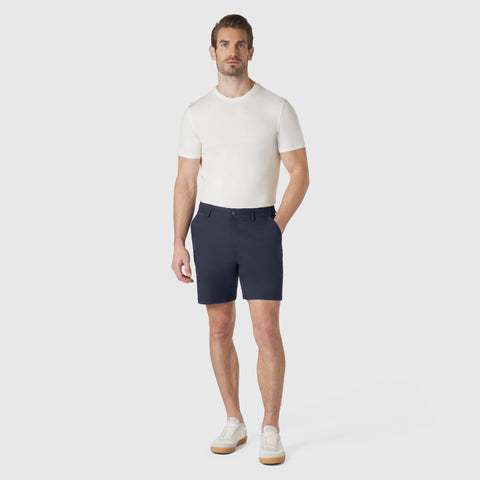 Man wearing Jetsetter Tech Short in navy blue, paired with a white t-shirt and white sneakers, standing against a neutral background.