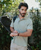 Man holding a golf bag outdoors with greenery in the background