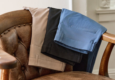 Four pairs of performance pants in khaki, black, blue and navy folded over a leather armchair.