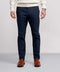 A man stands against a plain background, wearing Jack Archer's Jetsetter Tech Pant in navy—sleek, wrinkle-resistant—paired with a white sweater, brown dress shoes, and a watch. The image is cropped at the shoulders to show only his lower half.
