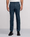 Against a plain background, a person wears Jack Archer's teal Jetsetter Tech Pant—water-repellent and wrinkle-resistant—paired with a white tucked-in shirt and black dress shoes. The photo is cropped from the shoulders down.