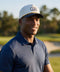 A man wearing the Archer Rope Hat in Cool Gray on the golf course