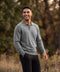 A man in a heather grey long-sleeve knit polo standing outdoors among trees and tall grass.
