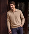 A man in a mocha heather long-sleeve knit polo leaning against a dark wood wall.