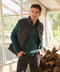 A green quarter-zip pullover layered under a black quilted vest in a greenhouse.