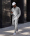 A man in a heather gray crewneck sweatshirt and matching sweatpants walking down a city street.