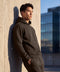 A man in an espresso brown hooded sweatshirt and joggers leaning against a concrete wall outdoors.