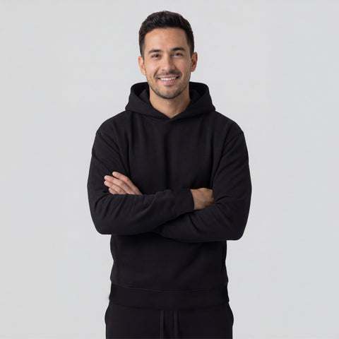 Man wearing a black hoodie with arms crossed on a light gray background