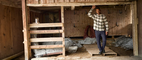 Man standing in barn wearing plaid button up shirt and navy tech pants from Jack Archer