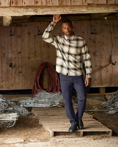 Man standing in barn wearing plaid button up shirt and navy tech pants from Jack Archer