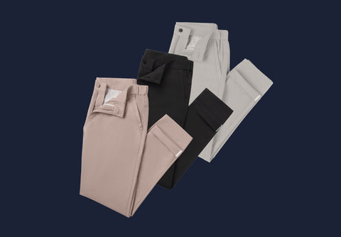 Four pairs of folded trousers in beige, black, and light gray, arranged diagonally on a dark navy blue background.