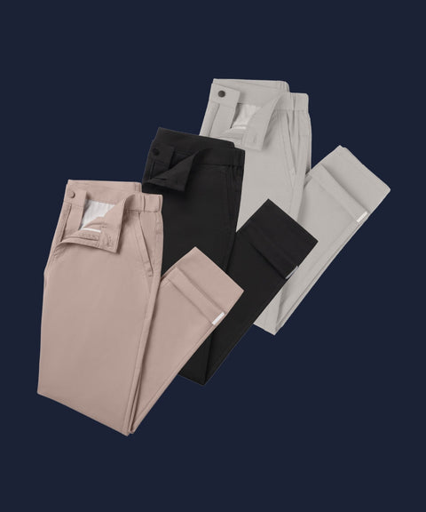 Four pairs of folded trousers in beige, black, light gray, and off-white, arranged diagonally on a dark navy blue background.