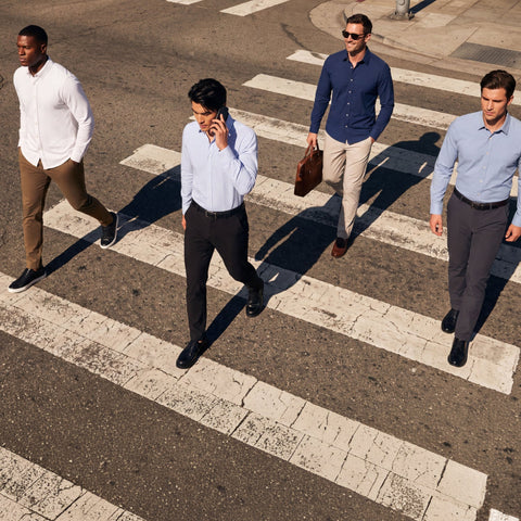 Four men in business casual attire walking across a city crosswalk on a sunny day, viewed from an elevated angle.