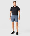 Man wearing Jetsetter Tech Short in blue, paired with a black polo shirt and black shoes.