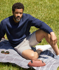 Man wearing Jetsetter Tech Short sitting on a picnic blanket outdoors with a football and sunglasses nearby.