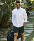Man wearing Jetsetter Tech Short with white shirt, standing outdoors, holding a black bag.