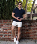 Man wearing Jetsetter Tech Short, leaning against a brick wall outdoors.