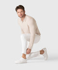 Man wearing Legacy Polo Sweater in beige, squatting with white pants and shoes.