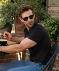 Man wearing Tech Polo, sitting outdoors, drinking coffee.