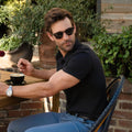 Man wearing Golf Game Essentials attire, featuring a deep blue polo and pants, seated outdoors with coffee.