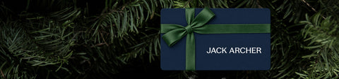 A navy Jack Archer gift card tied with a green ribbon bow, resting on evergreen branches.