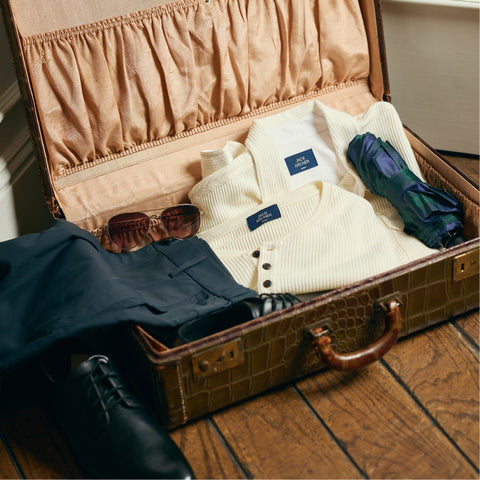 An open vintage suitcase packed with cream waffle henleys, navy pants, sunglasses and an umbrella.