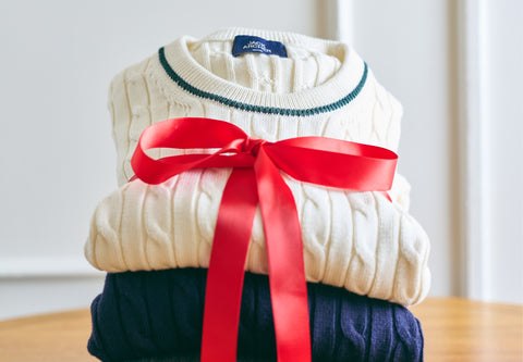 A stack of cream and navy cable-knit sweaters tied with a red gift ribbon.