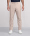A man stands against a light gray background wearing Jack Archer’s Jetsetter Tech Pant in beige, paired with a tucked-in dark navy shirt and white sneakers.
