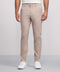 A person wears Jack Archer's Jetsetter Tech Pant Slim Fit in Oak Khaki with white sneakers, standing against a plain light gray background. Only their lower torso and legs are visible; the upper body is mostly out of frame.