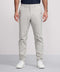 A man wears Jack Archer Jetsetter Tech Pant Relaxed Fit in Sand Stone with a dark tucked-in shirt and white sneakers, standing with arms at his sides against a plain background. Only his upper body is partially visible.