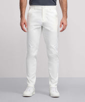 A person wearing white Jack Archer Jetsetter Tech Pant with white sneakers and a dark shirt stands against a light gray background, showing only the lower half of the body.