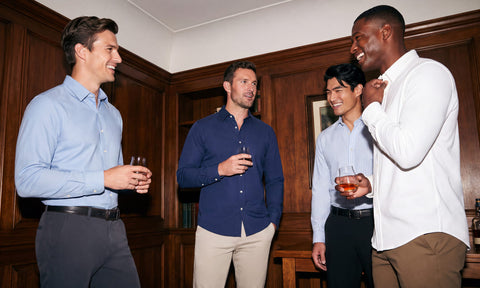 Four men in Everywear Shirts holding drinks and chatting in a wood-paneled room