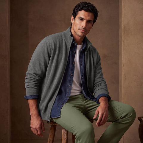 A grey full-zip sweater layered over a chambray shirt and white tee with olive chinos.