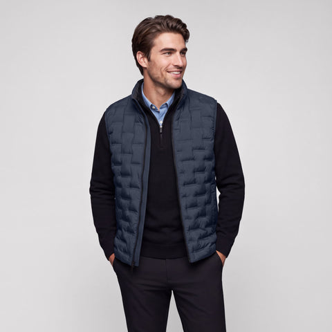 Deep blue quilted Drive vest worn open over a black quarter-zip sweater.
