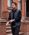 A man in the deep blue quilted Drive vest walking past a brownstone stoop.