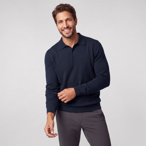 A navy knit long-sleeve polo worn with charcoal trousers.