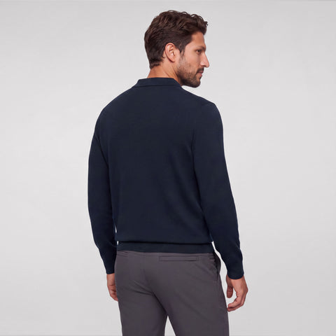 Back view of a navy knit long-sleeve polo worn with charcoal trousers.