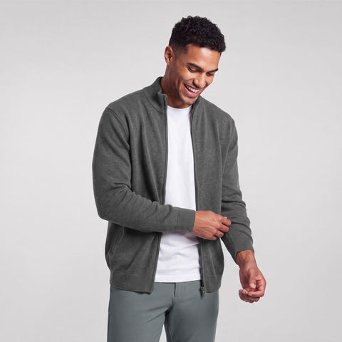 A model in a heather gray full-zip sweater over a white tee, adjusting the cuff.