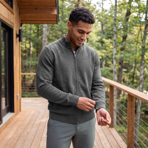 A man in a heather gray full-zip sweater on a wooden deck surrounded by trees.