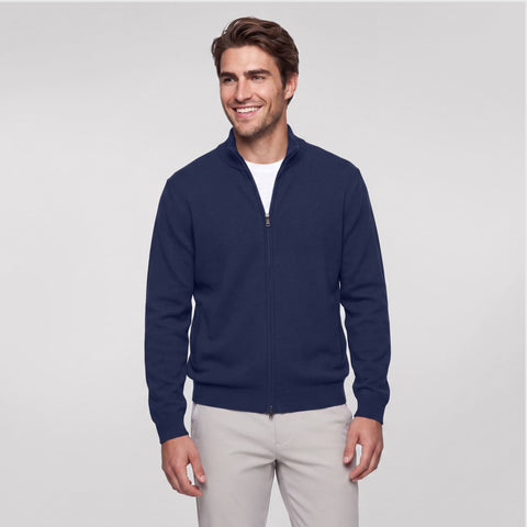 A man wearing a navy full-zip sweater over a white tee with stone chinos.