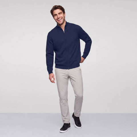 A man in a navy full-zip sweater, stone chinos and black sneakers, full length.