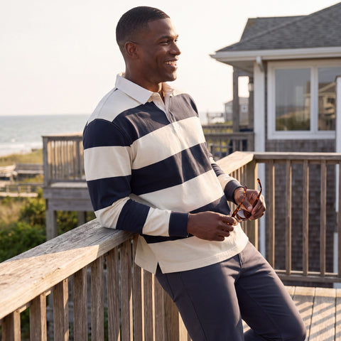 A navy and cream striped rugby polo worn with charcoal trousers on a beachfront deck.