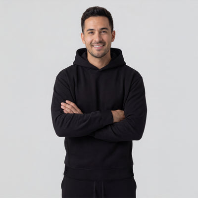 Man wearing a black hoodie with arms crossed on a light gray background